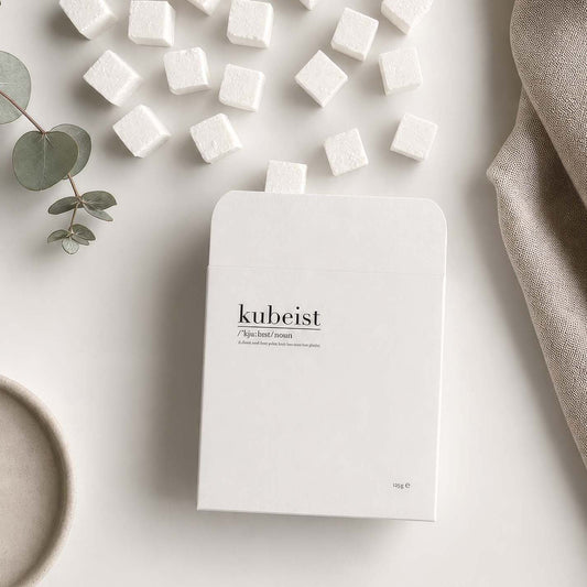 Kubeist product packaging on a light surface with scattered shower cubes cubes and greenery.